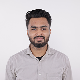 A man with a beard and styled hair wearing a light gray button-up shirt 